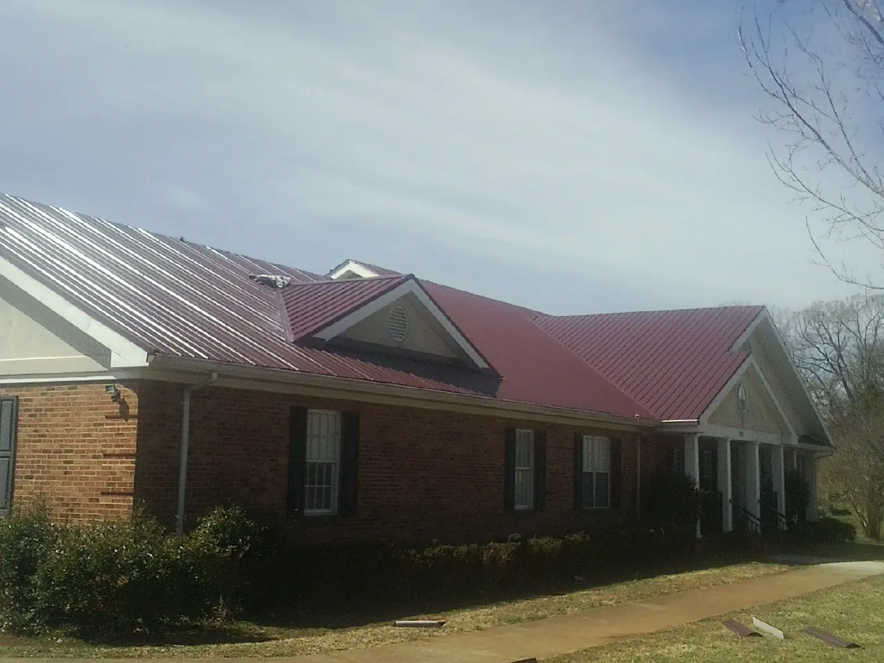 Red metal roof with gabled entries on a long brick building, from a Hail Damage Roof Repair job in Palos Verdes Peninsula