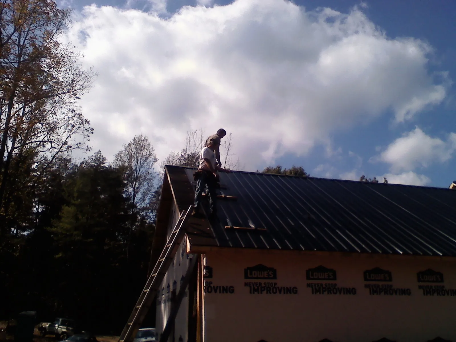 Roofer fastening dark metal panels high against a cloudy sky, from a Roof Inspection job in Palos Verdes Peninsula
